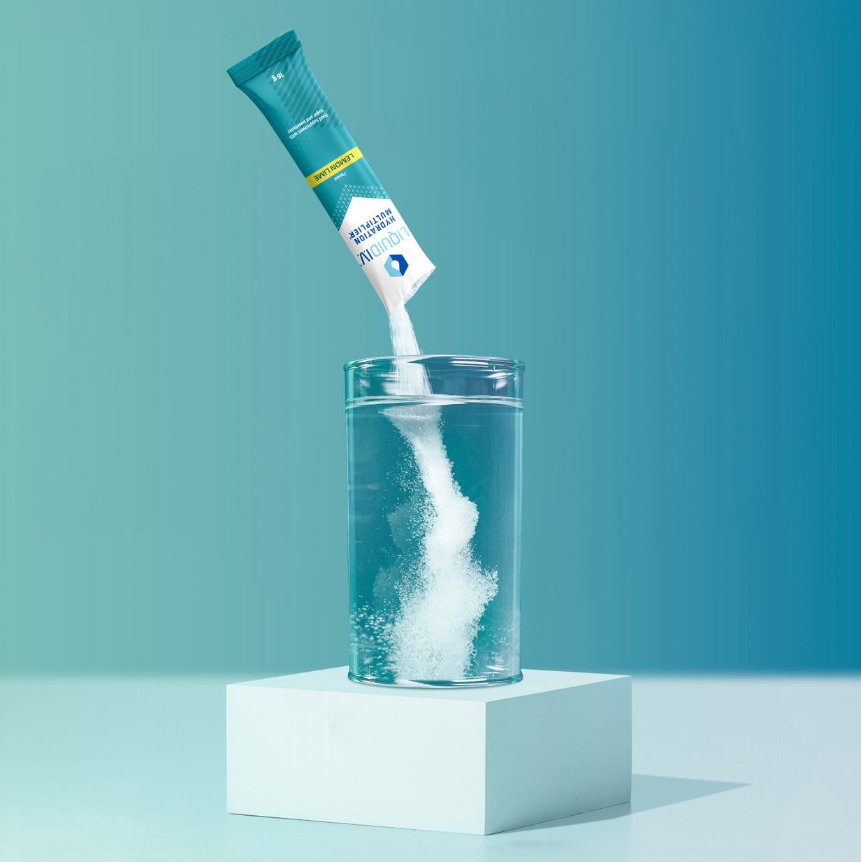 Liquid I.V. Hydration Multiplier Lemon-Lime powder being poured into a glass of water on a white pedestal with a gradient blue background