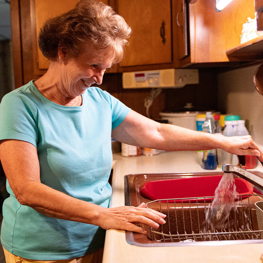 Smiling woman washing dishes in her kitchen, using clean running water